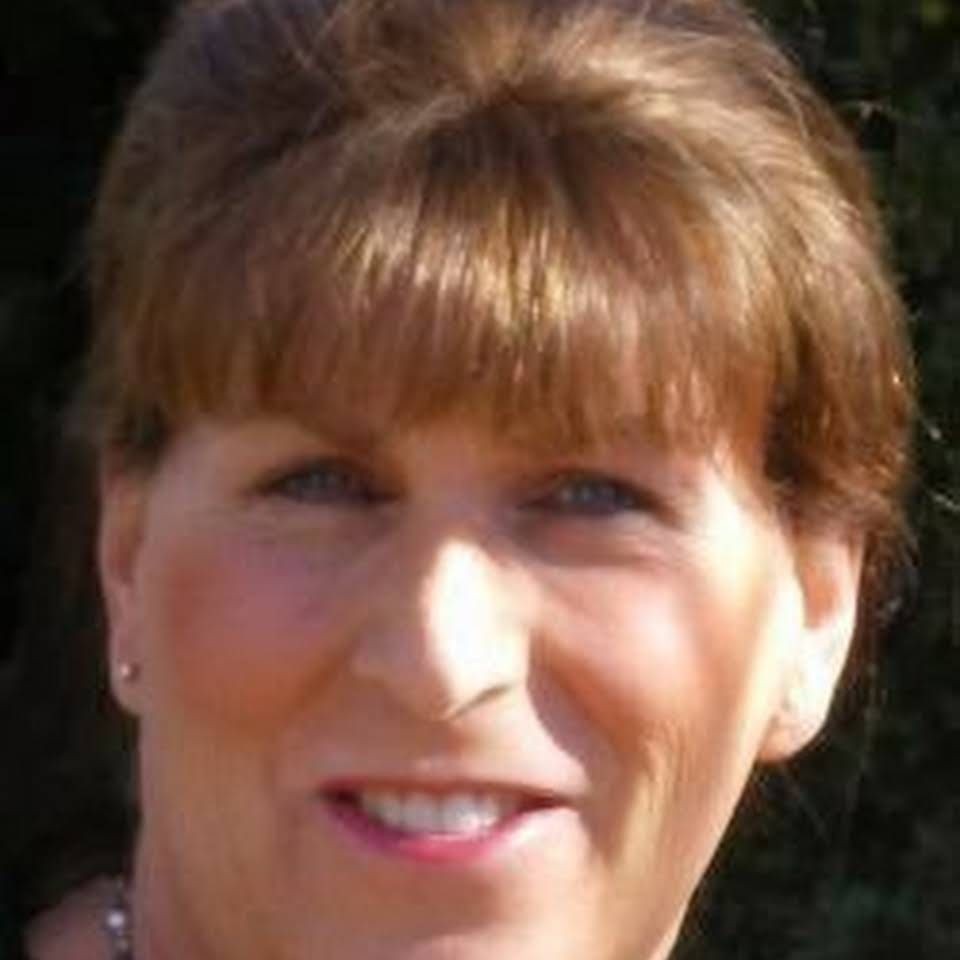 Close-up of a person with brown hair smiling against a dark background.