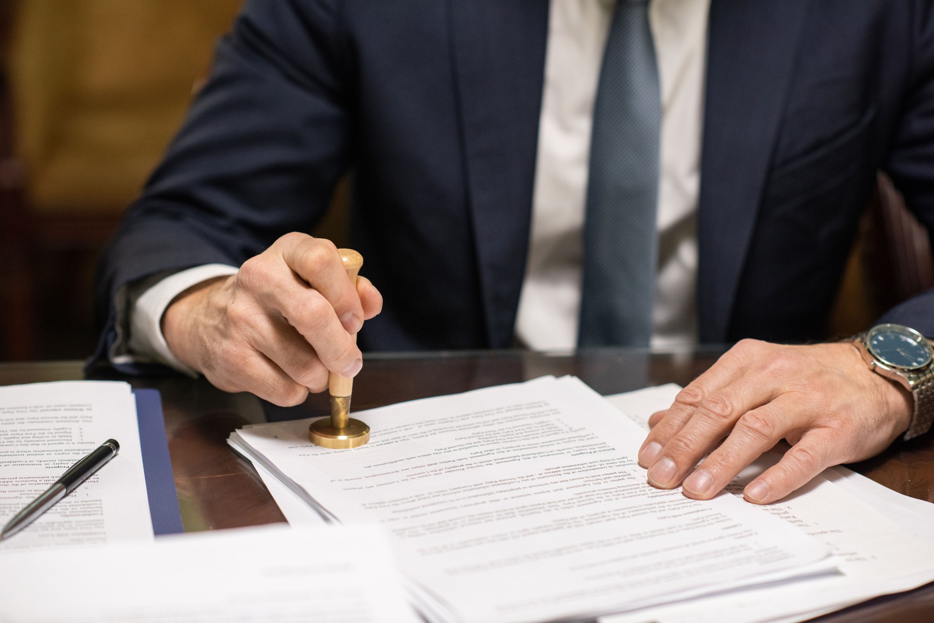 Hands of director in elegant suit putting stamp on approved document